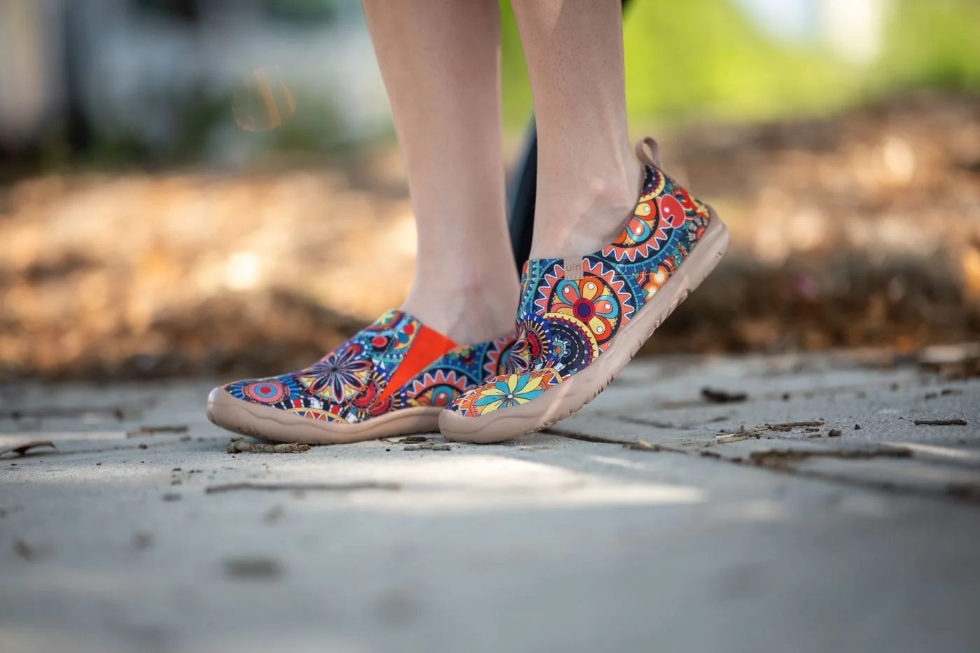 Colourful patterned shoes worn on a sunny pavement.
