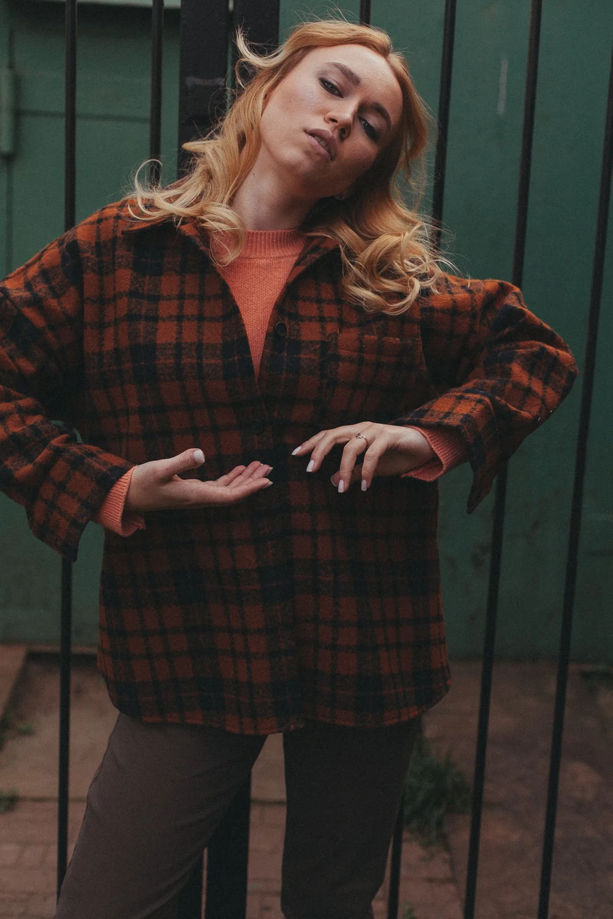 A woman wearing an open checkered overshirt over a knit outdoors.
