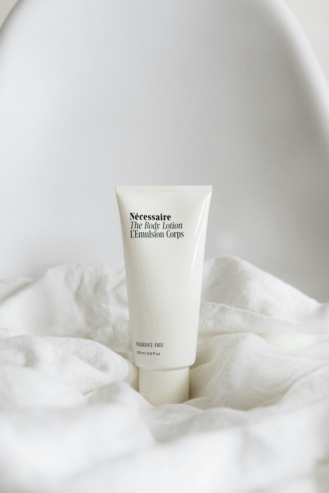 A pale cosmetic tube standing on rumpled pale bedding.
