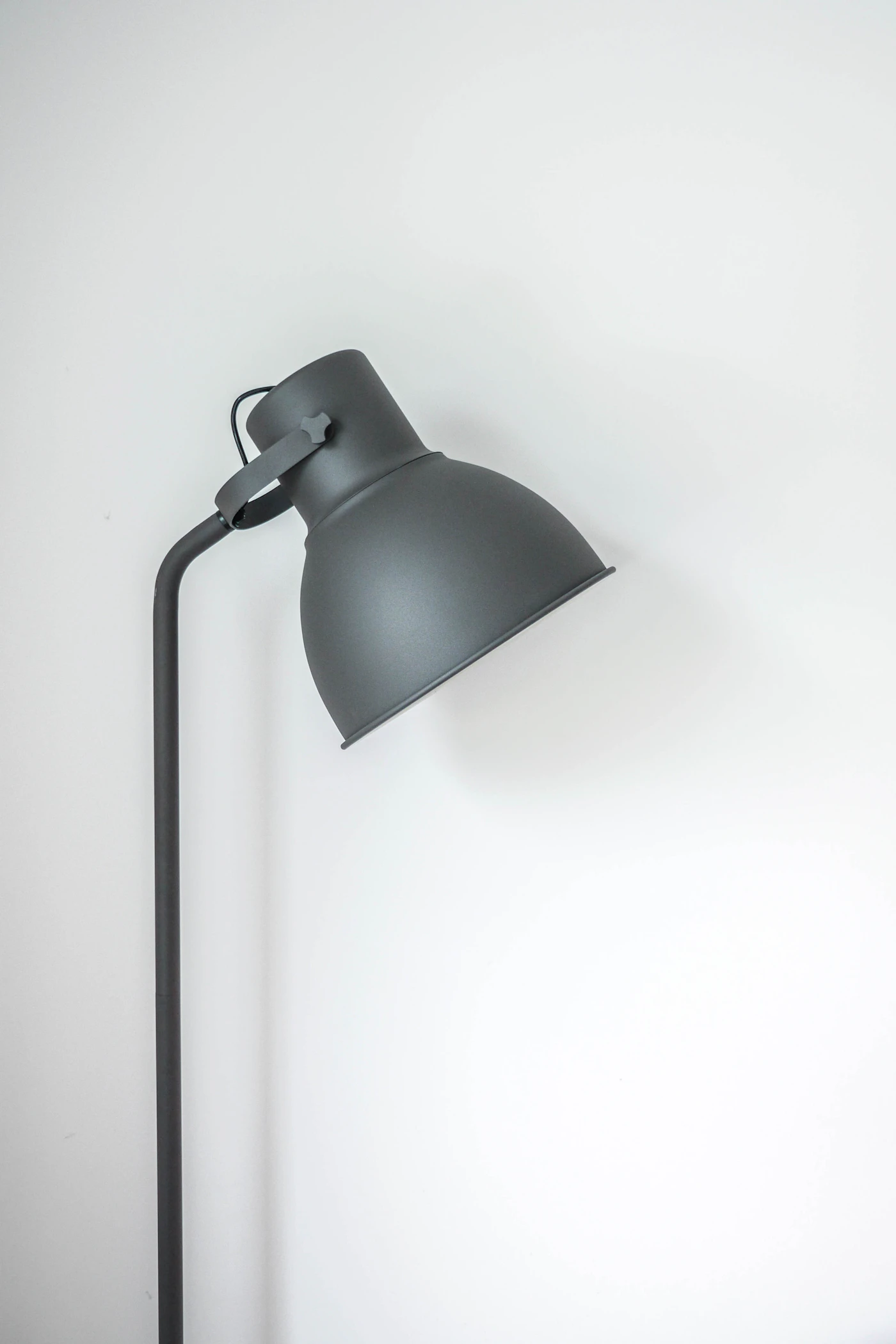 A dark adjustable task lamp against a pale wall.