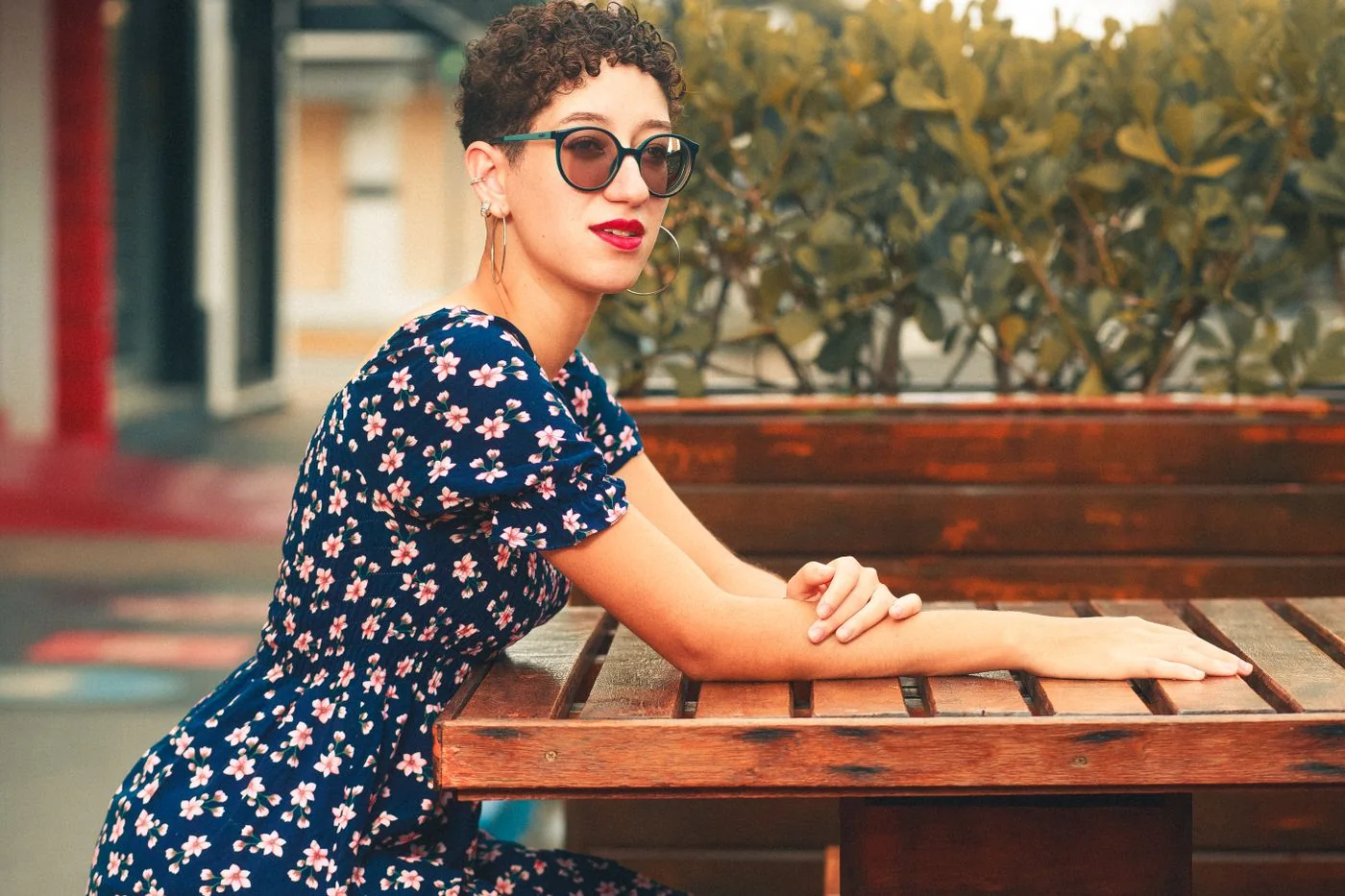 A woman in a dark floral dress and sunglasses beside an outdoor table.