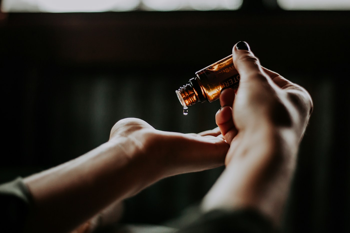 Hands holding an amber-coloured bottle beside an outstretched wrist.