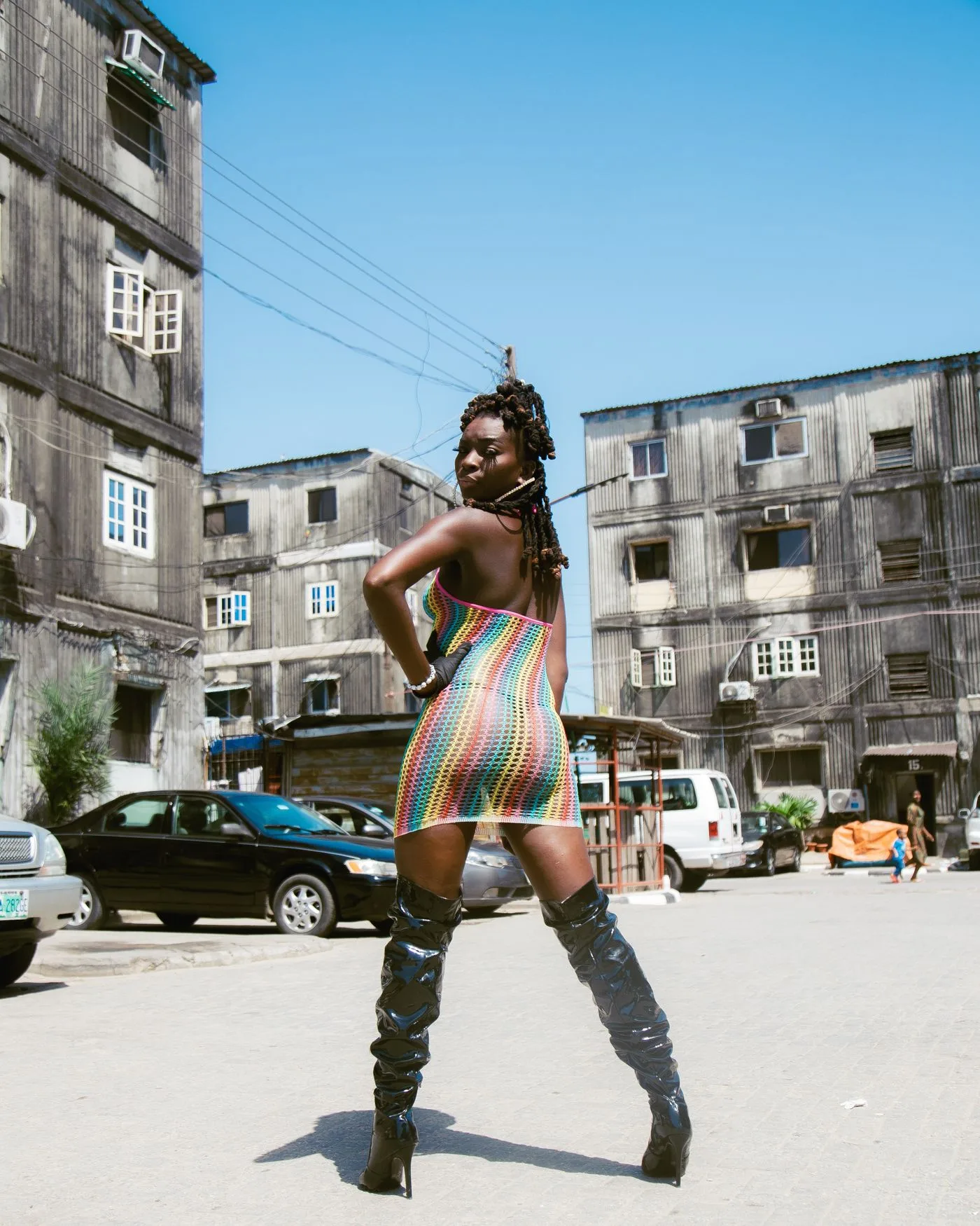 A woman in a multicoloured dress and tall dark boots on a city street.