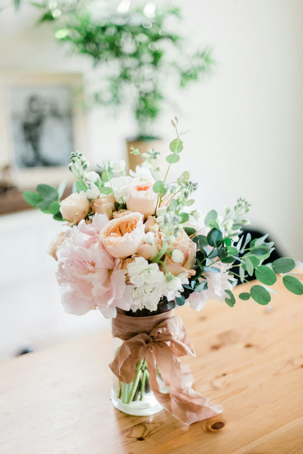 Pale pink and white flowers in a clear vase on a wooden surface.