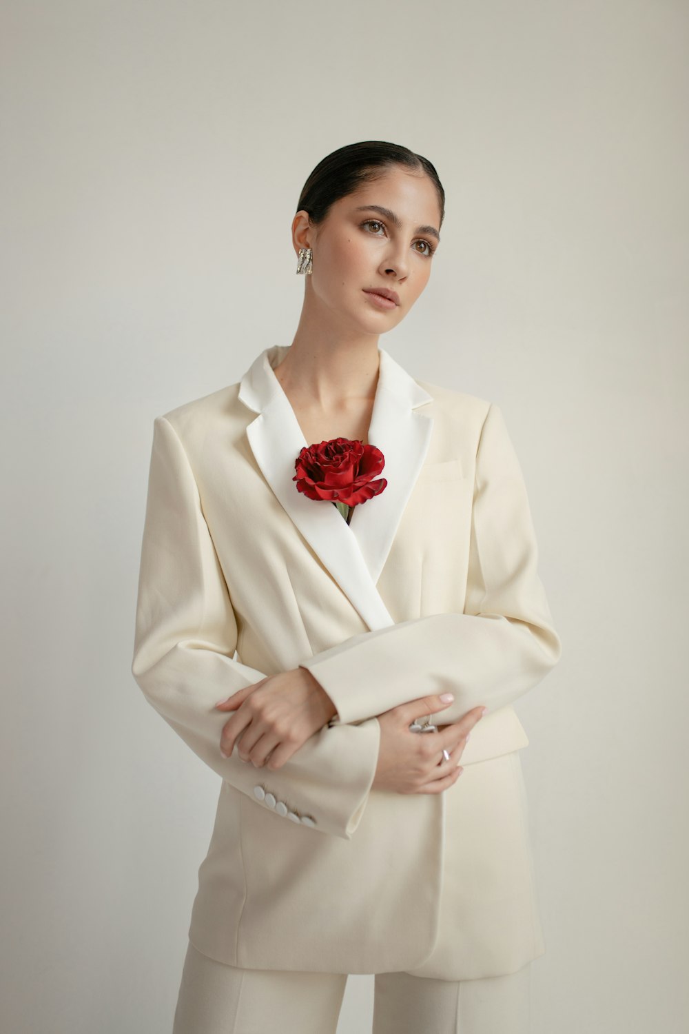 A woman in a pale tailored jacket with a red floral detail near the neckline.