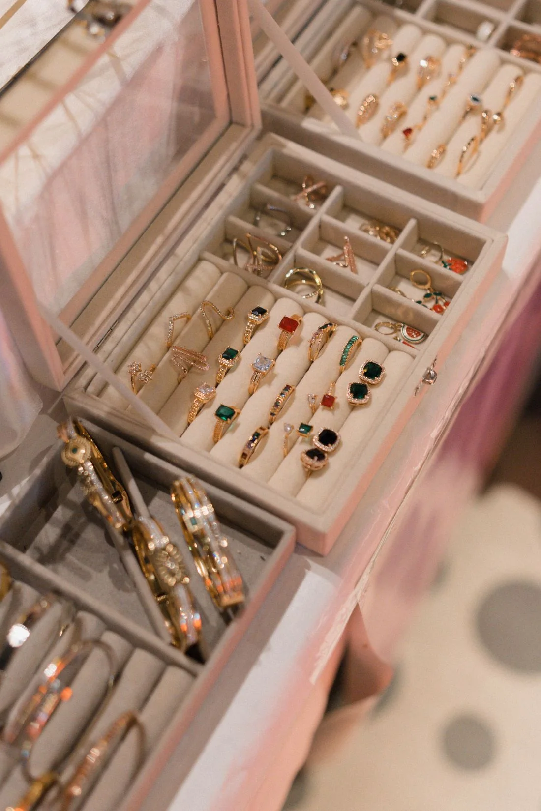 An open pale jewellery box holding rings, bracelets and other pieces.