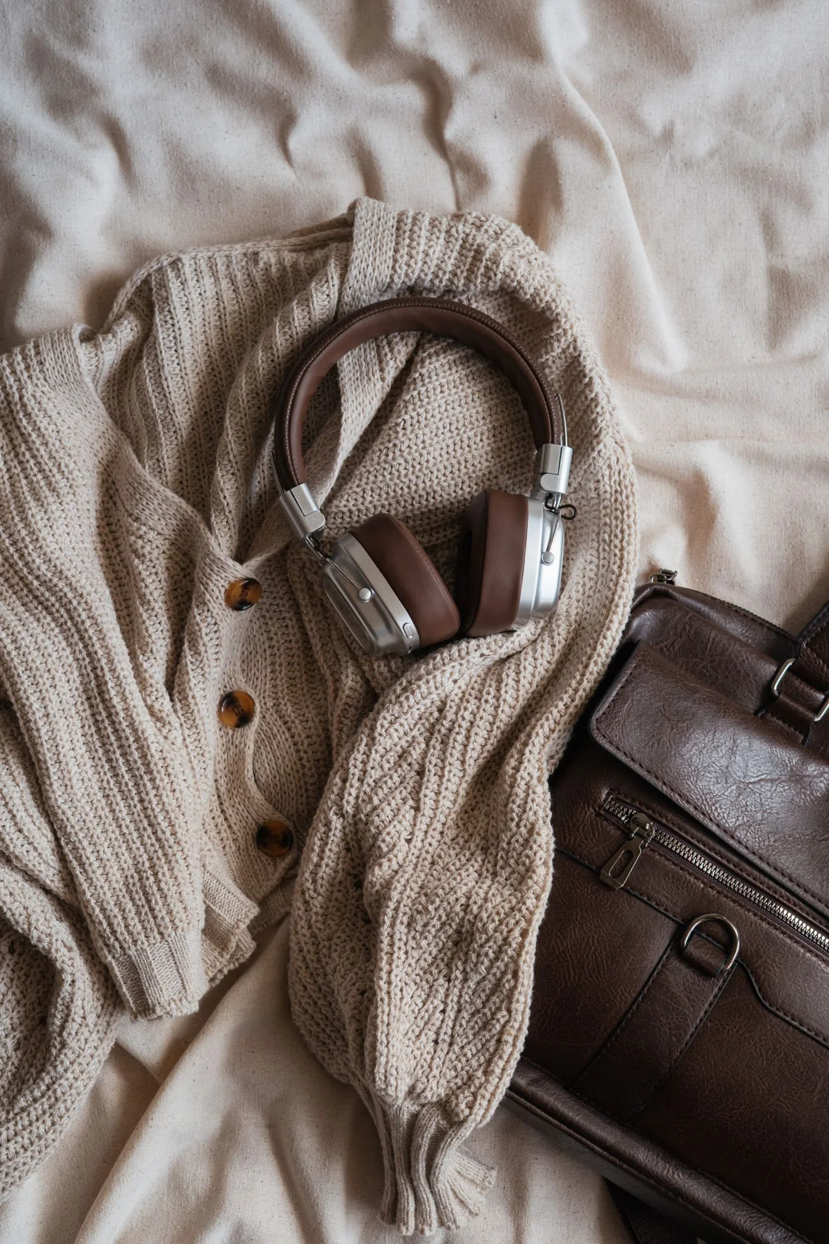Headphones on a pale knitted garment beside a brown bag.
