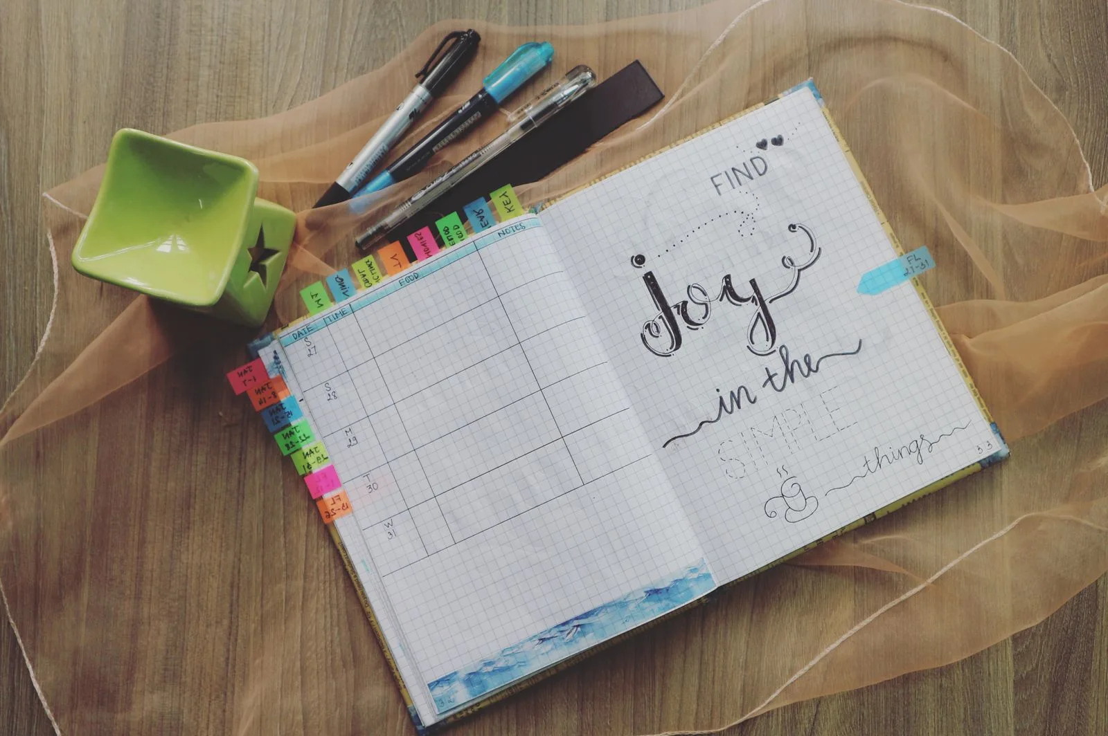 An open planner with colourful tabs and pens on a wooden surface.