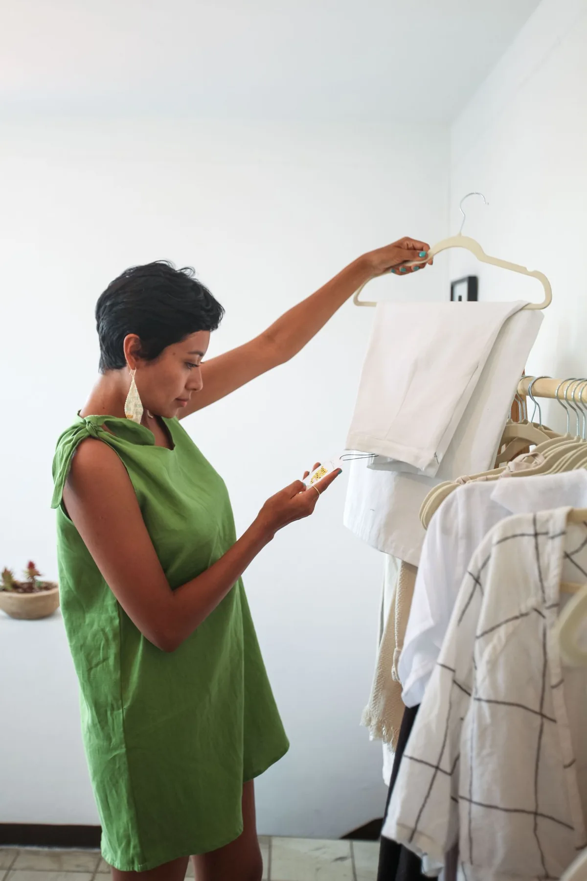A woman holding a pale garment on a hanger beside a clothes rail.