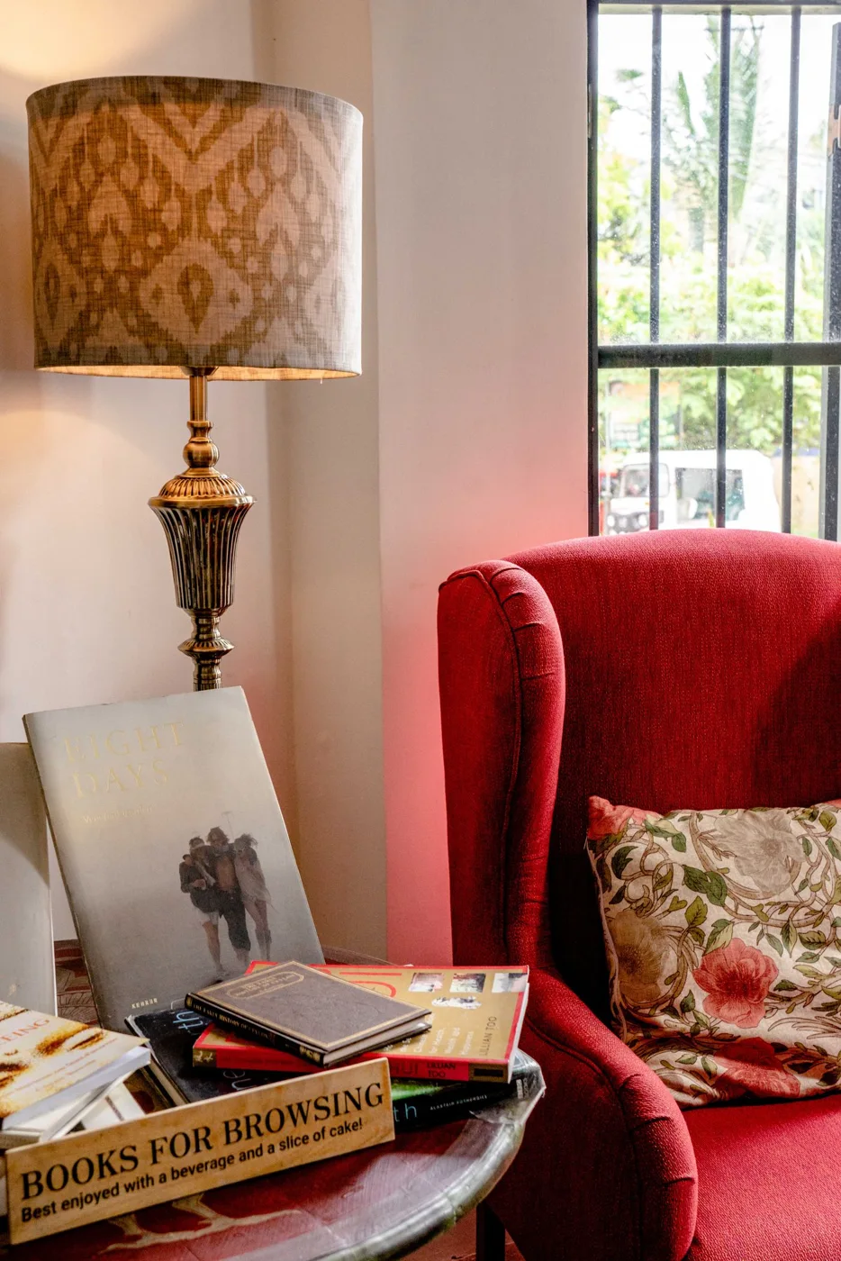 A red armchair beside a floor lamp and a table with books.
