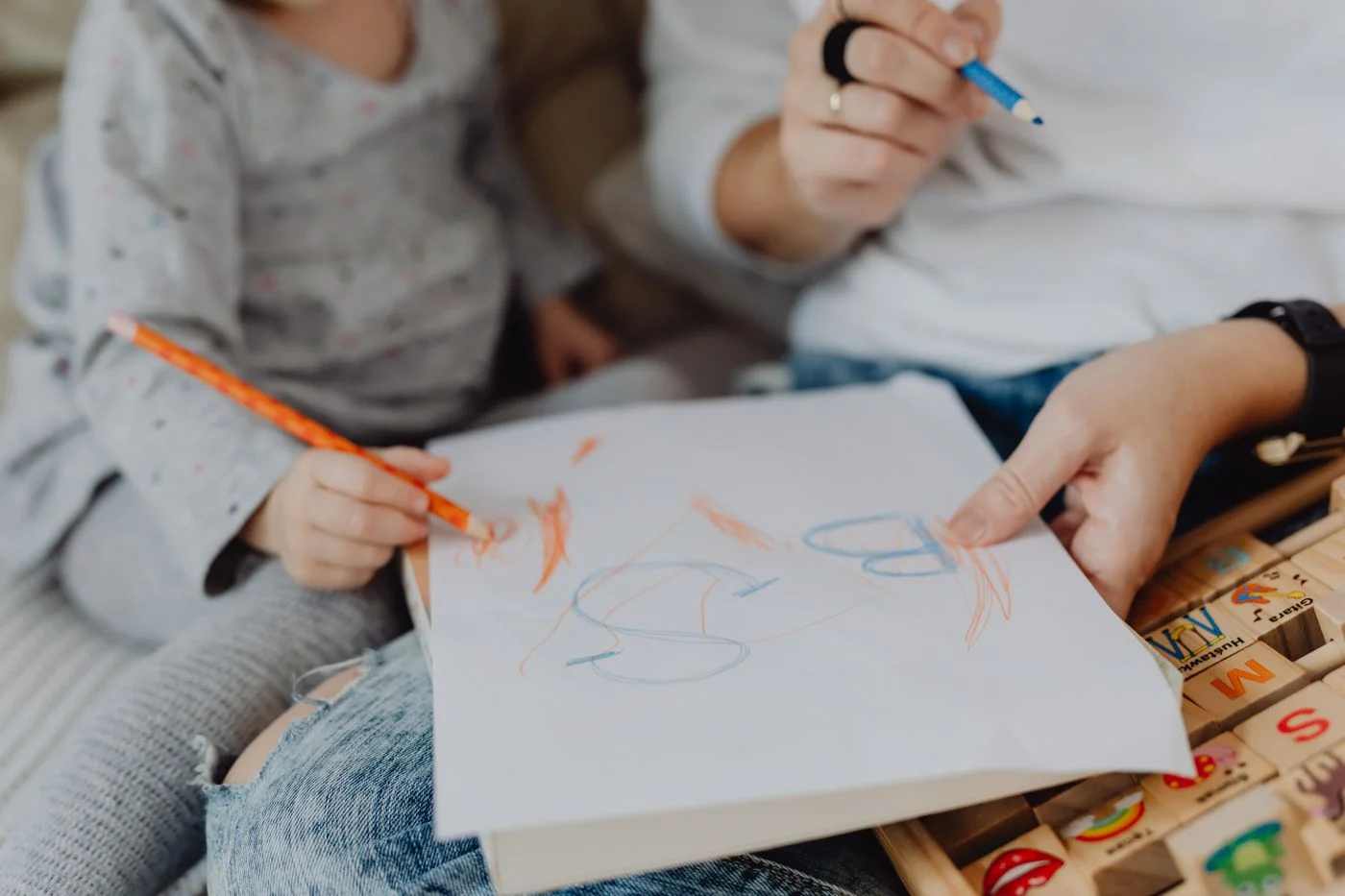 An adult and child drawing together with crayons on paper.