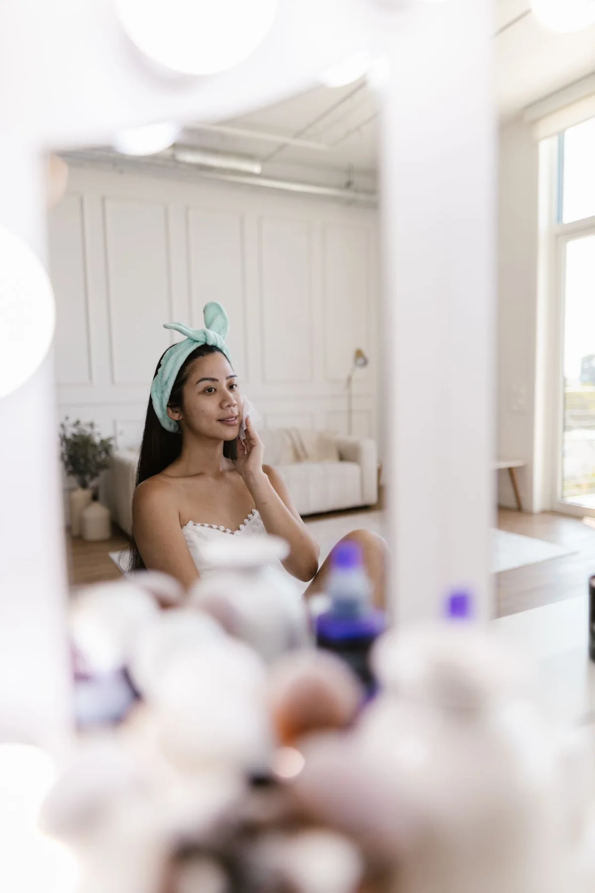 A woman wearing a headband looking at herself in a wall mirror.