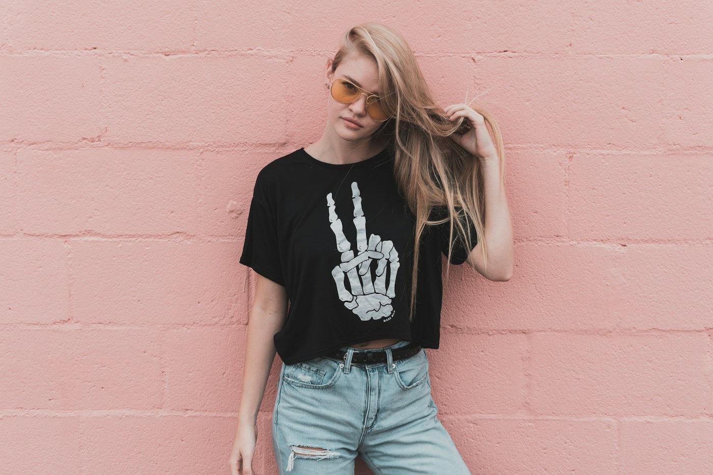 Woman in a black T-shirt and light denim shorts beside a pink wall