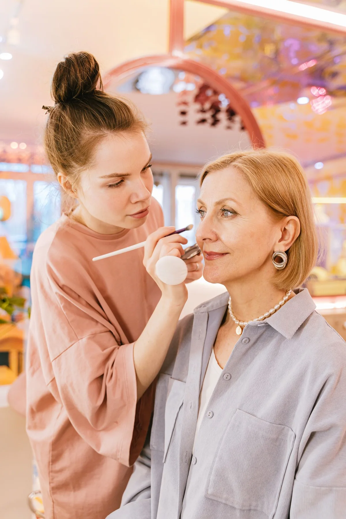 A makeup artist applying cosmetics to a seated client in a salon.