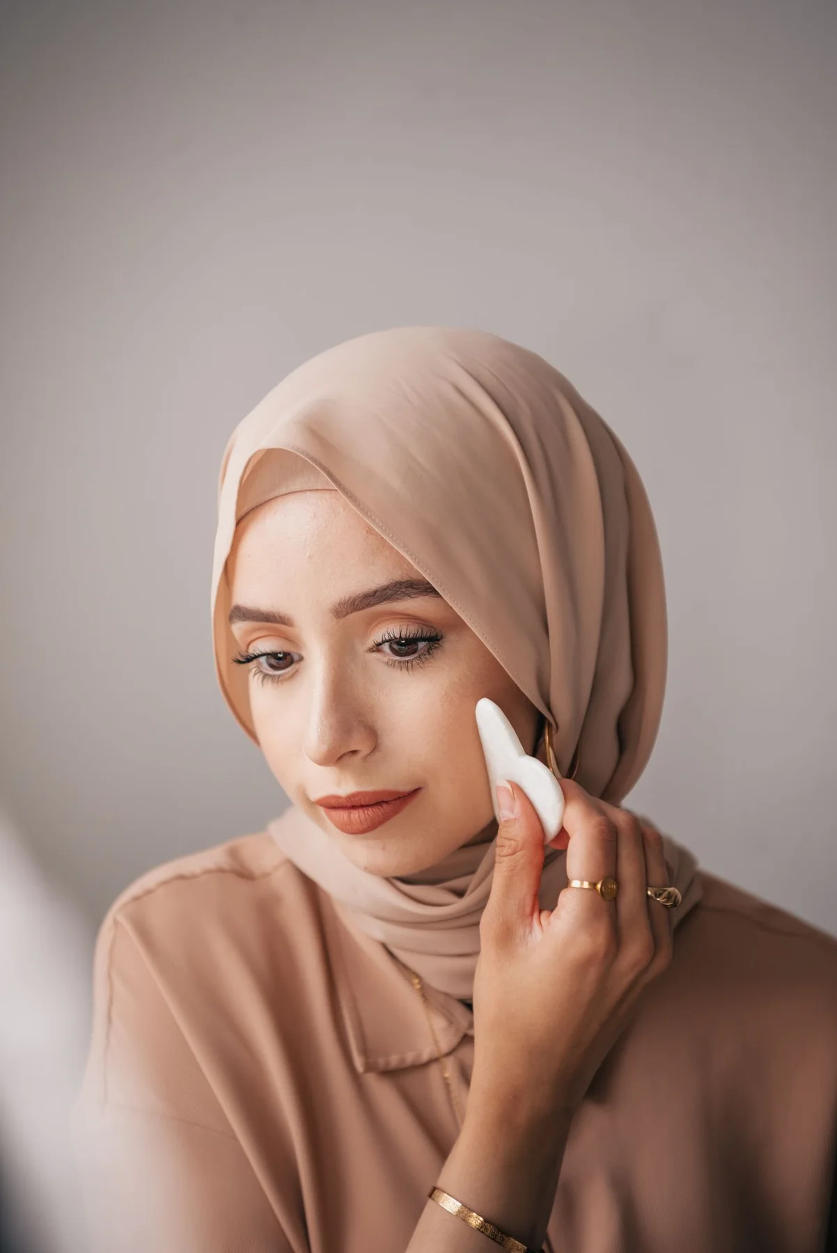 A woman wearing a headscarf applying makeup with a sponge.