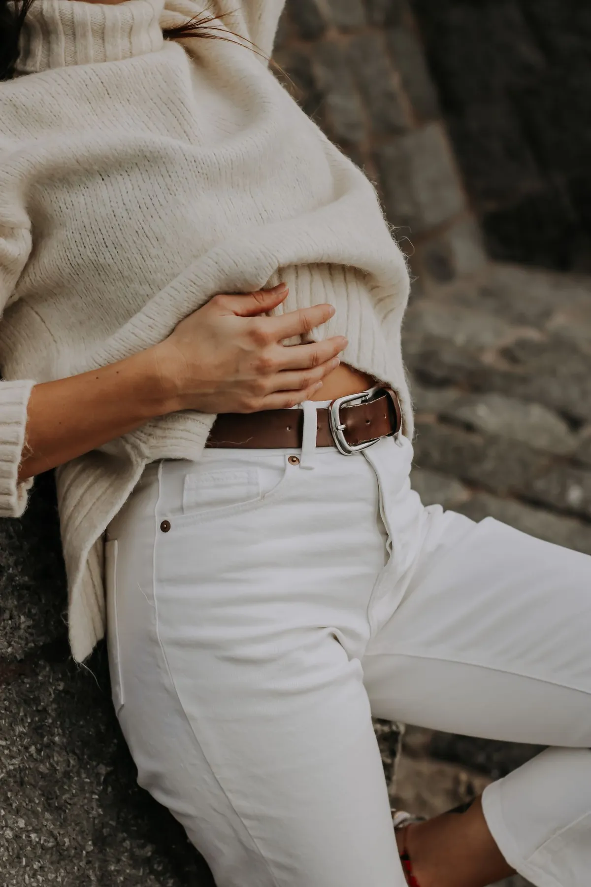A close view of a sweater, white jeans and a brown belt worn together.