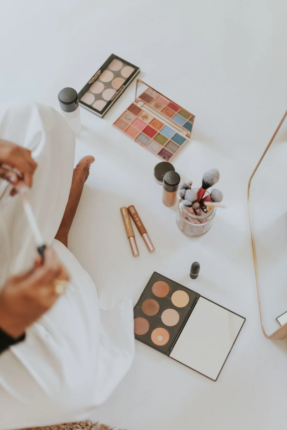 Palettes, bottles and brushes on a pale dressing surface beside a person.