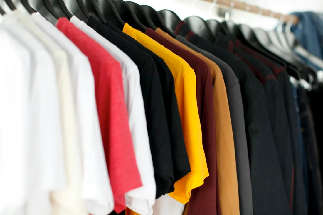 Plain T-shirts in several colours grouped on hangers.