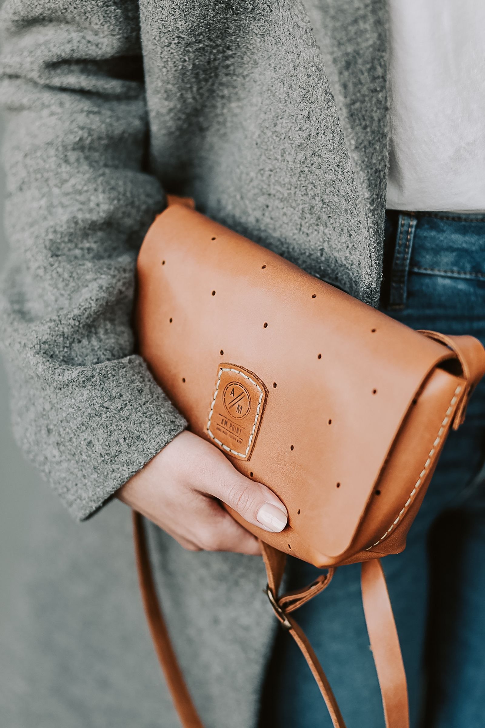 A tan handbag held beside a grey coat.
