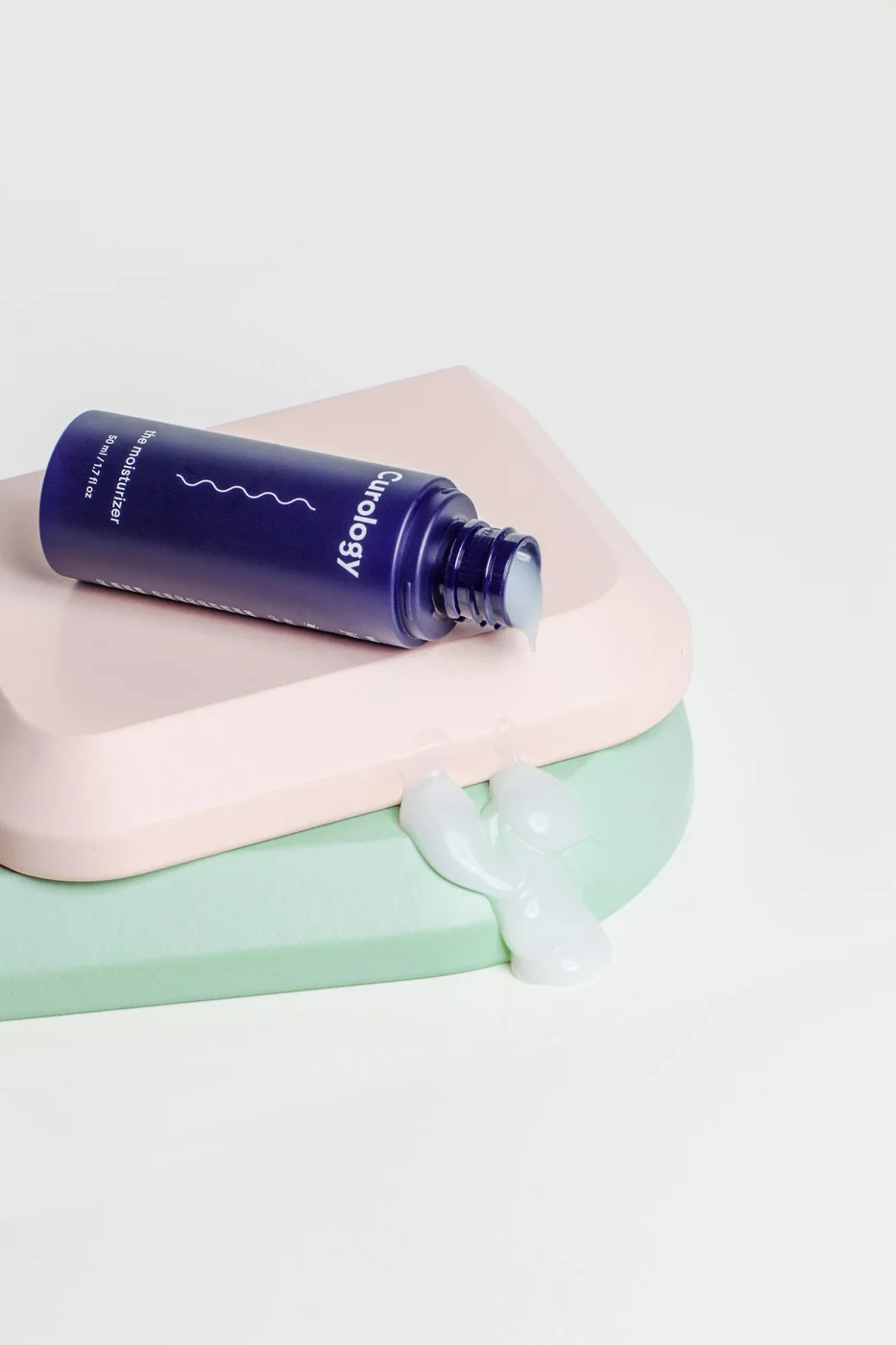 A purple cosmetic bottle resting on pale rectangular display blocks.