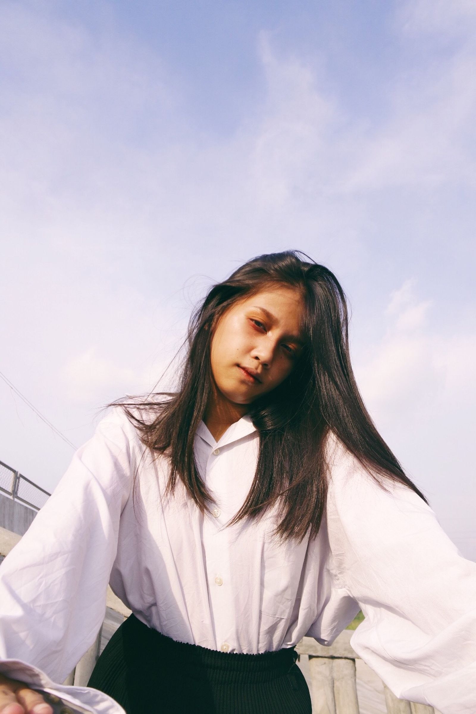 A woman wearing a pale full-sleeved blouse outdoors.