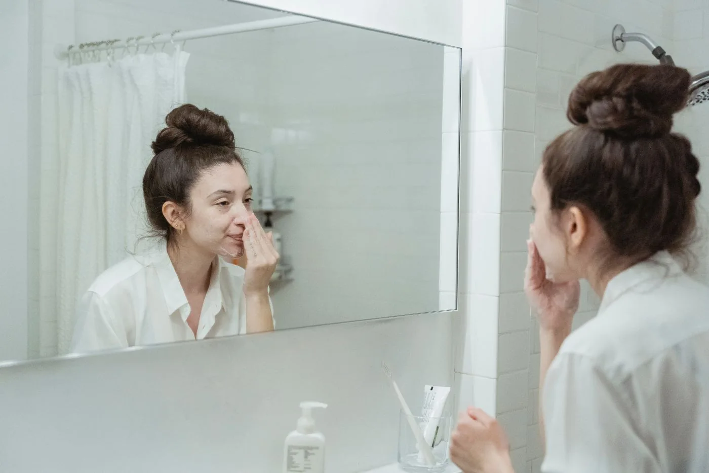 A woman looking into a bathroom mirror with her hand near her face.