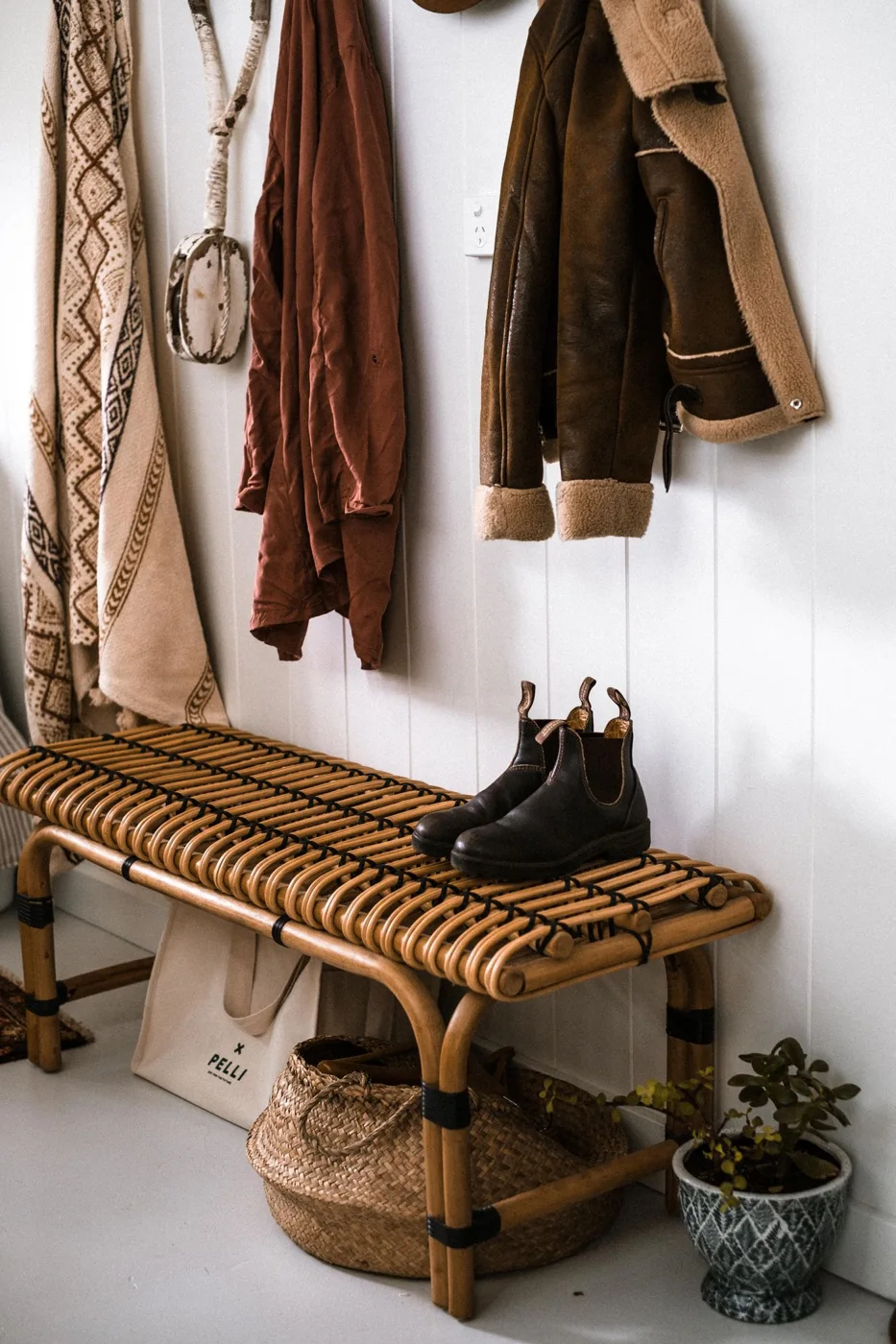 Coats hanging above a woven bench in an entryway.